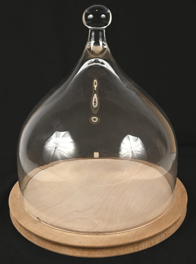 Een kaasstolp van geblazen glas, op ronde houten basis.