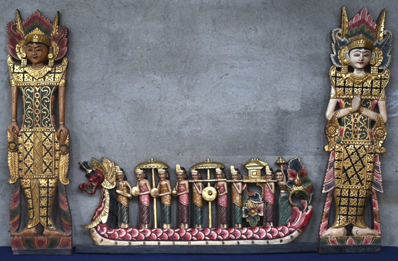 Drie gepolychromeerde houten decoratievoorwerpen. Twee tempeldansers en een drakenboot met muzikanten.
