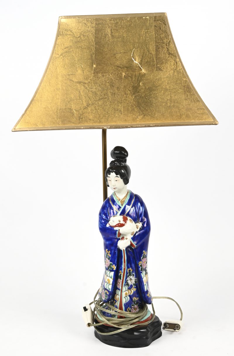 Tafellamp met een beeld van Chinees porselein. Een jonge vrouw in kimono met een hondje. Goudkleurige kap en houten basis.