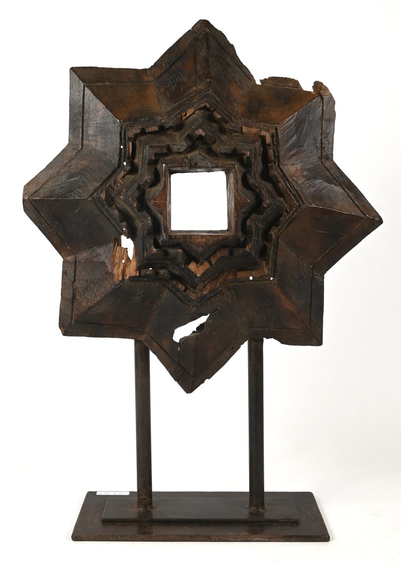 Een oude gesculpteerde massief eikenhouten ornament op metalen presenteersokkel.