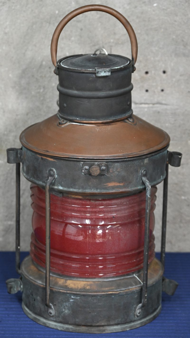 Een oude koperen scheepslamp met rode lens (bakboord). Omgebouwd naar elektriciteit, de oude olielamp is nog aanwezig.