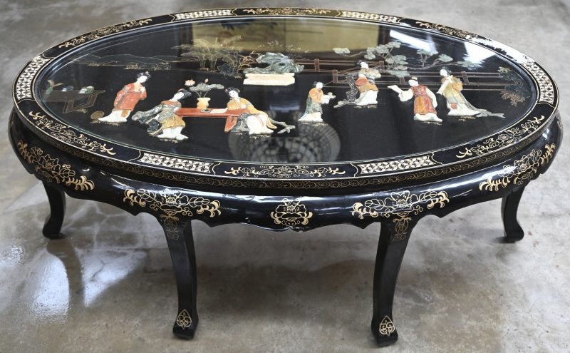 Een ovale Chinese salontafel van zwartgelakt hout met een decor van pietra dura onder glas.