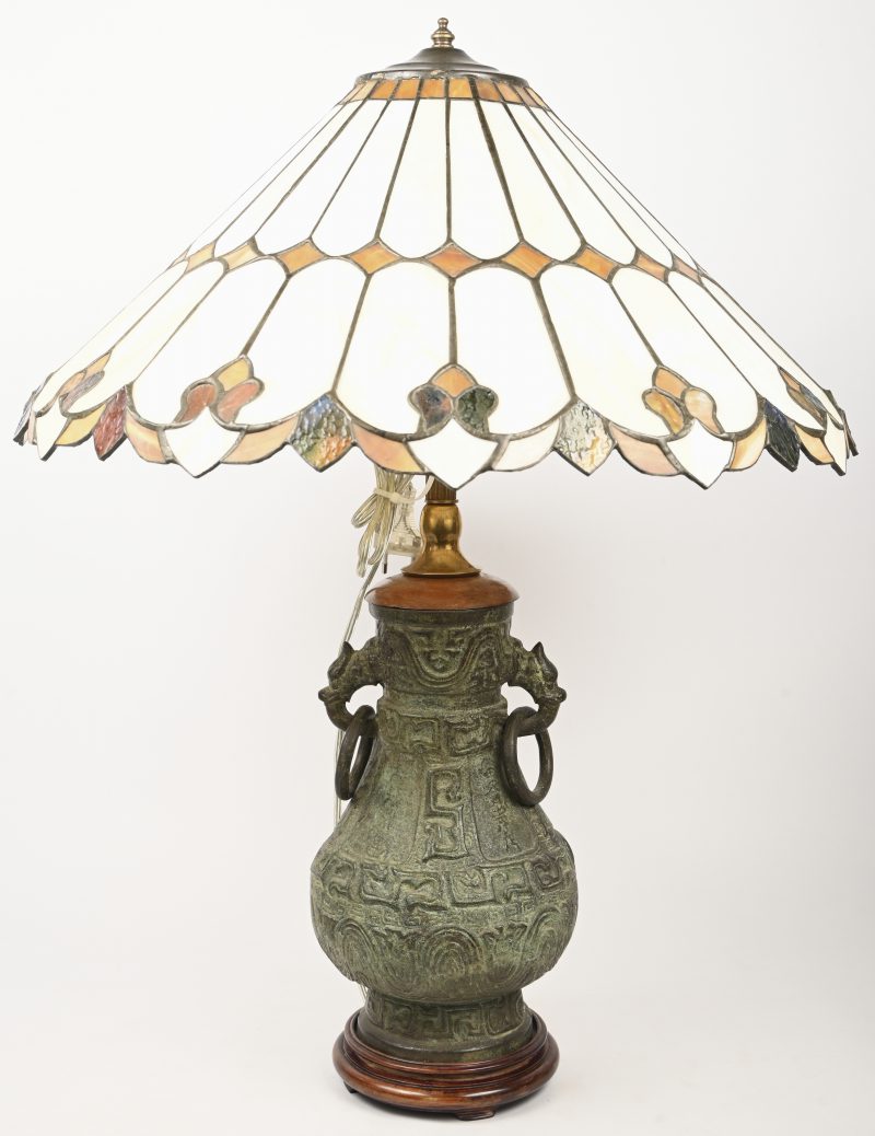 Een tafellamp op een Chinese, bronsgepatineerde kruik en een lampenkap in Tiffany stijl.