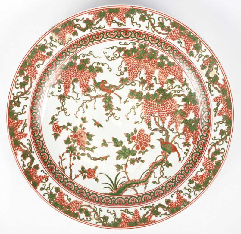 Een groot sierbord van Chinees porselein, versierd in groen en rood met vogels en druivenranken.