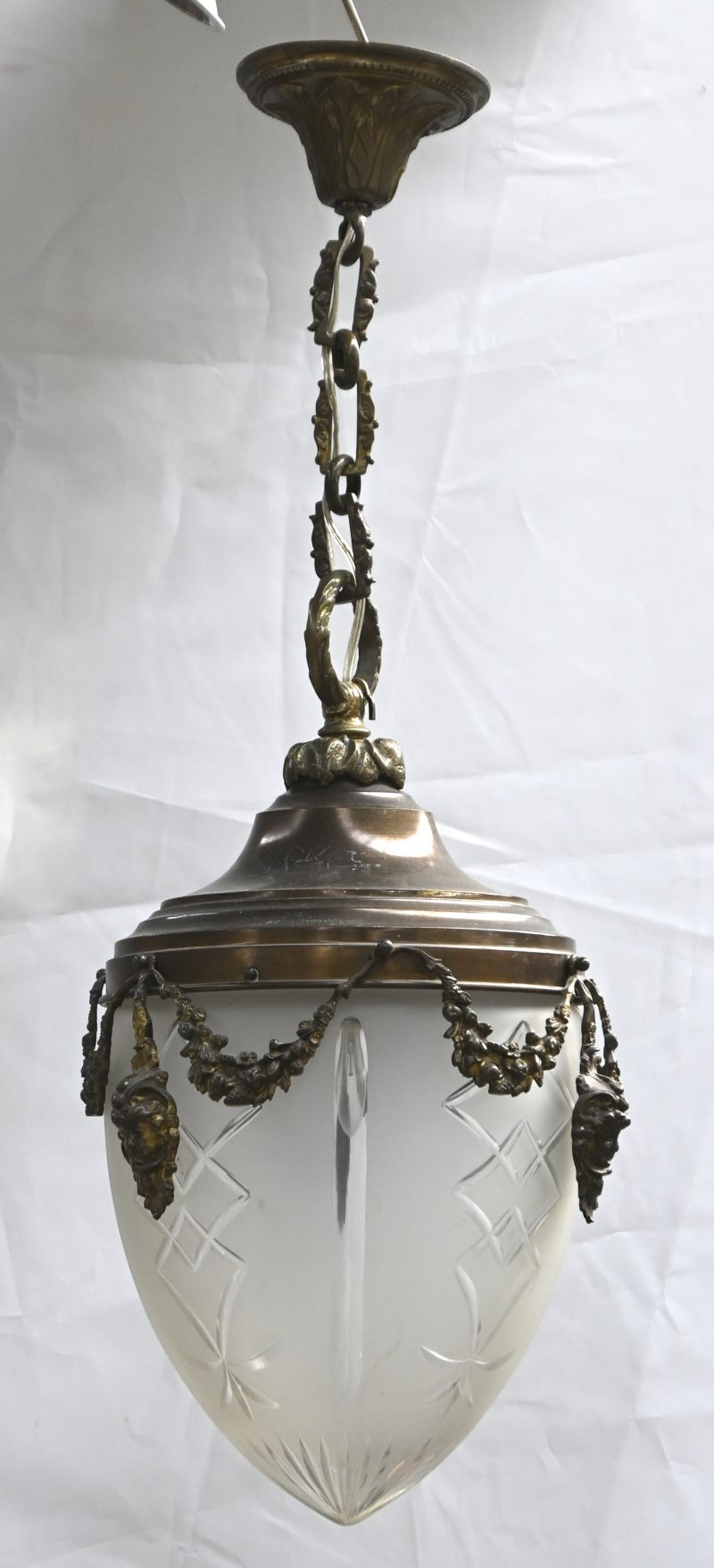 Grote hanglamp met geslepen opaalglazen coupe. Koperen kap versierd met hoofdjes en guirlandes.