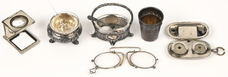 Een zilveren borrelglaasje en een lot verzilverd metalen snuisterijen bestaande uit 2 miniatuur potjes, een antieke muntenhouder, een pince-nez en een drukkersloupe.