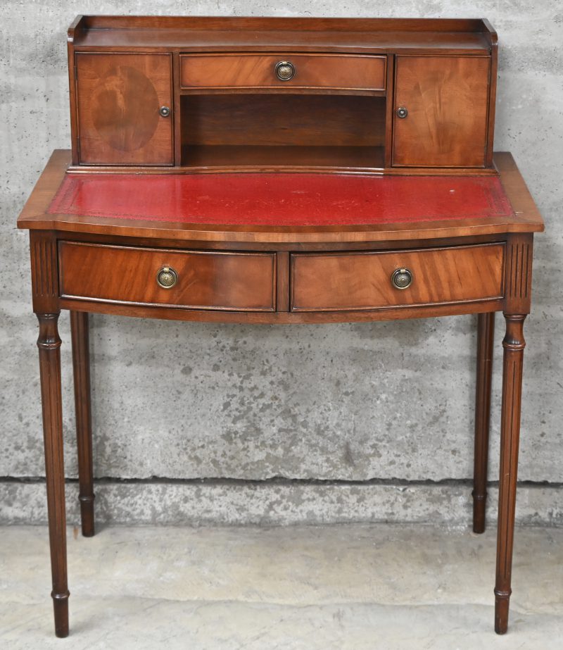 Schrijftafeltje met lage opzet en rood lederen blad, in klassieke stijl. Onderaan 2 laden en boven 1 lade en 2 deurtjes.