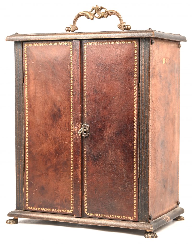 Een koffertje in de vorm van een twee deurs kast, met plaats voor één fles en vier borrelglaasjes. Met bronzen leeuwenpootjes en handvat, bekleed met rood leder.