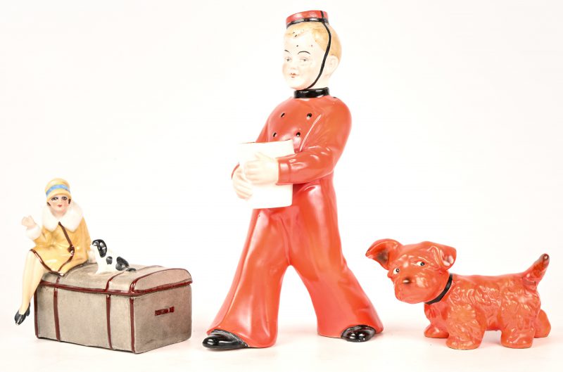 Een lot porselein met schade bestaande uit een art-deco karafje in de vorm van een piccolo, een hondje en een doosje met dame op een reiskoffer.