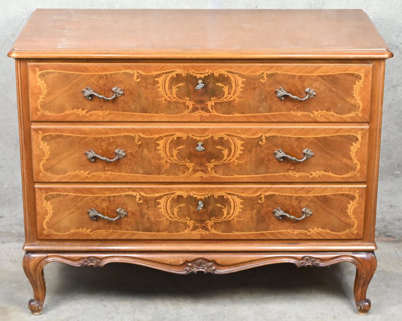 Een houten commode in Lodewijk XV stijl met drie laden en gemarquetteerde versiering.