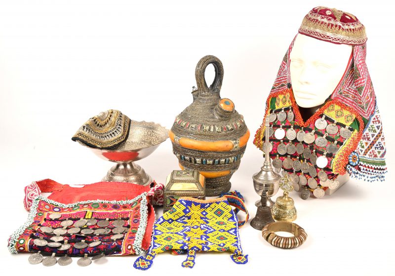 Een gevarieerd lot ethnische klederdracht en siervoorwerpen bestaande uit 5 kledingsstukken, een schenkkan, een schaal en een druppelaar in verzilverd metaal, een sierpotje, een armband en 2 belletjes.