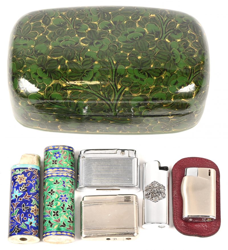 Een lot van drie vintage aanstekers en drie aanstekerhouders waarvan 2 van zilver. In een zwart gelakt doosje, beschilderd met groene bloemen. Het zilver heeft een brutogewicht van 35 gram.