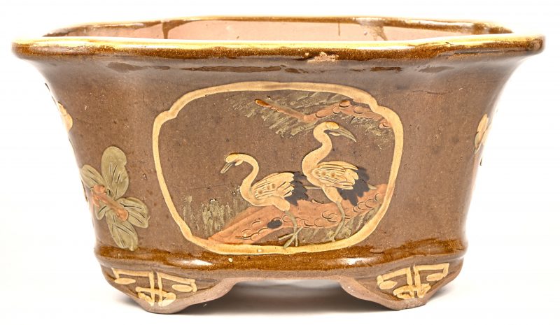 Grote okerkleurige bloempot van Chinees aardewerk. Gedecoreerd met kraanvogels, een hertje en bloemen. Minieme schilferschade aan de rand.