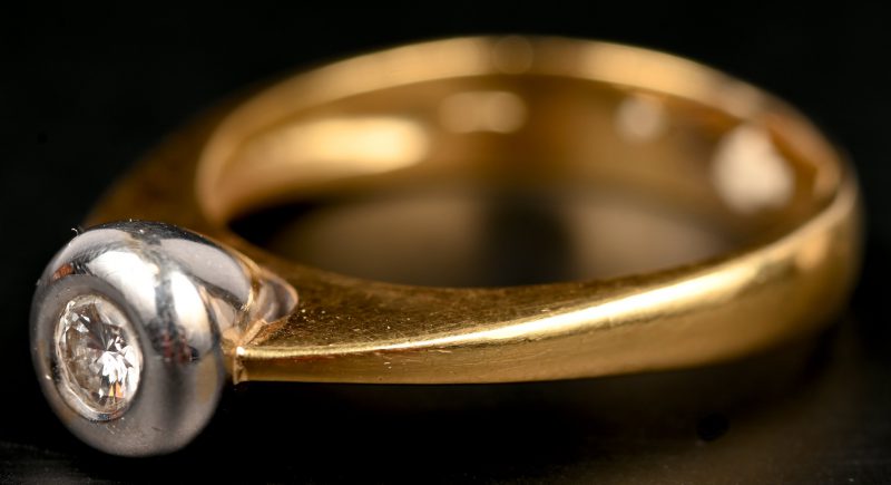 Een 18 kt wit- en geelgouden ring bezet met centrale briljant van 0,20 ct.