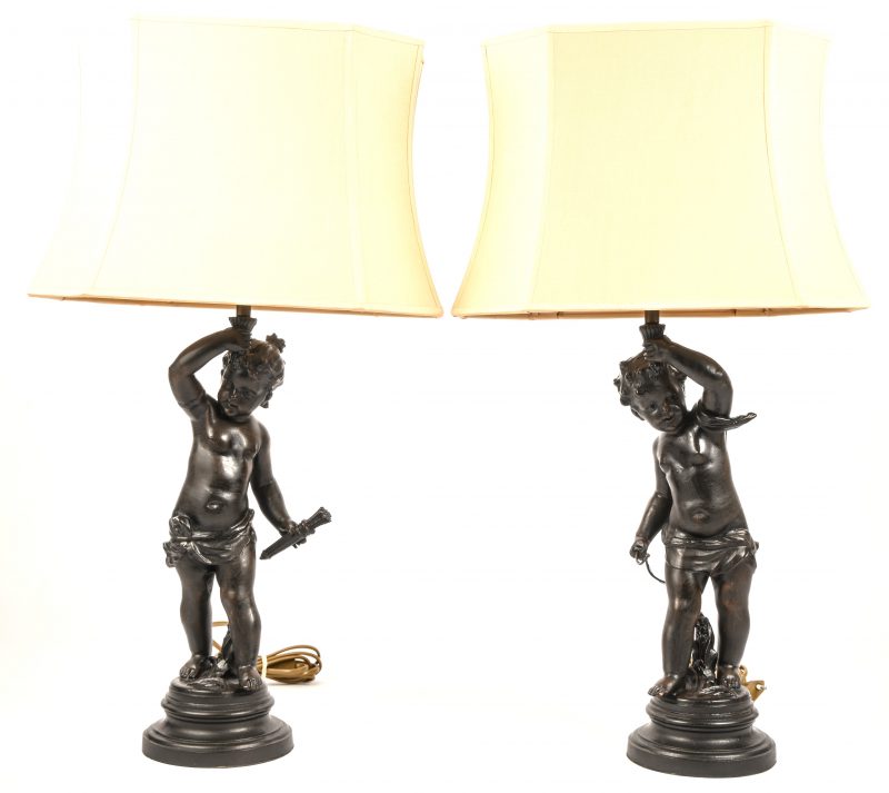 Een paar tafellampen gevormd als putti’s die een fakkel dragen. Zamak met beige stoffen lampenkap.