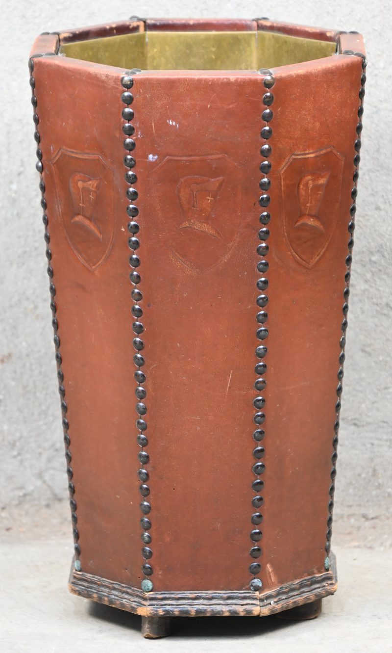 Een achthoekige houten paraplubak, met leder bekleed en gedecoreerd met wapenschildjes. Koperen inzet!