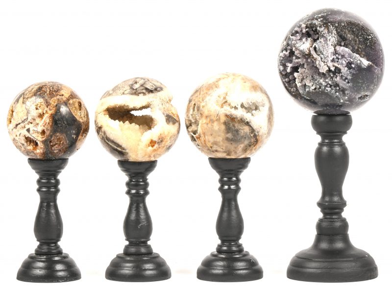 Een set van vier stenen ballen met mineralen en kristallen. Gepresenteerd op zwarte voetjes.