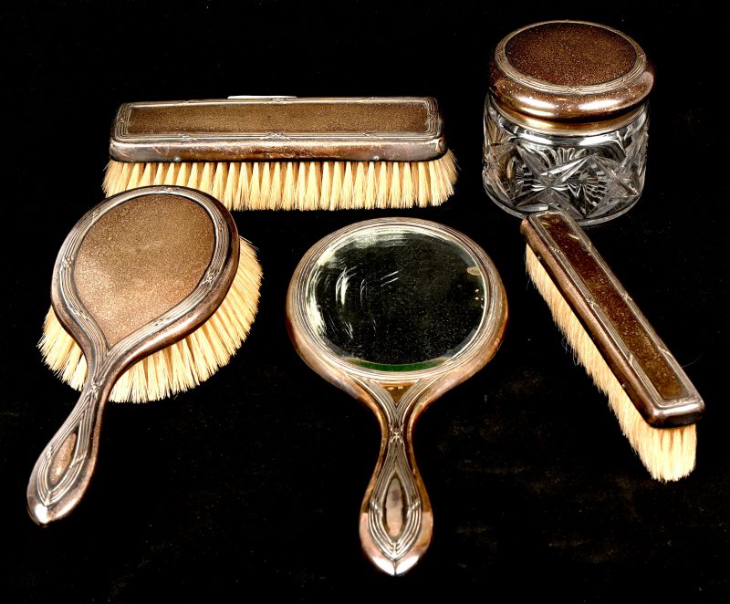 Een zilveren make-up set gemerkt Delheid, bestaande uit 3 borstels, een dekselpot, een handspiegel en de rand van een kam.