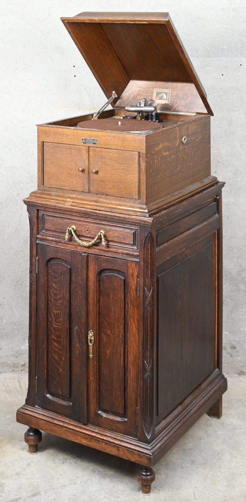 Een grammofoon, His Masters Voice, op bijhorend meubel en een partij 78-toeren platen. De opwindhendel ontbreekt.
