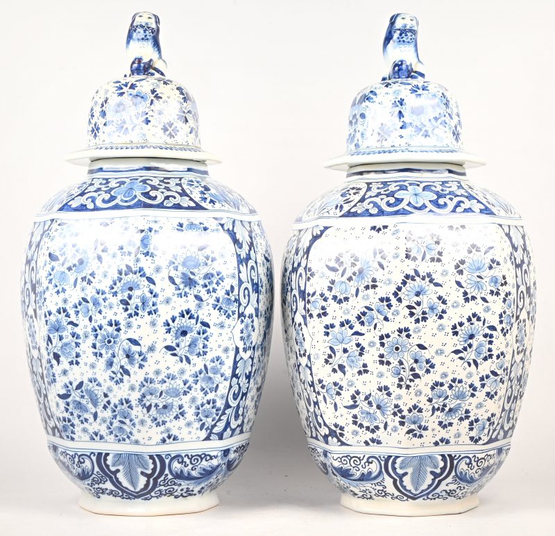 Een paar dekselvazen van blauw-wit aardewerk, met een decor van bloemen en een foo hond als dekselknop. Gemerkt; Royal Boch.