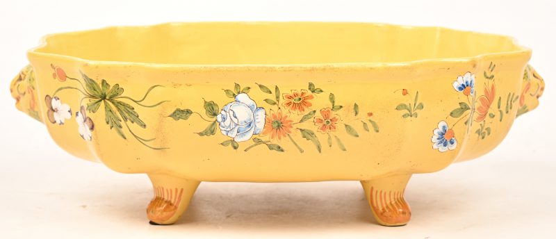 Een 18e eeuwse schaal op pootjes, van geel geglazuurd aardewerk. Met leeuwenkopjes en een decor van bloemen. Montauban, Frankrijk.