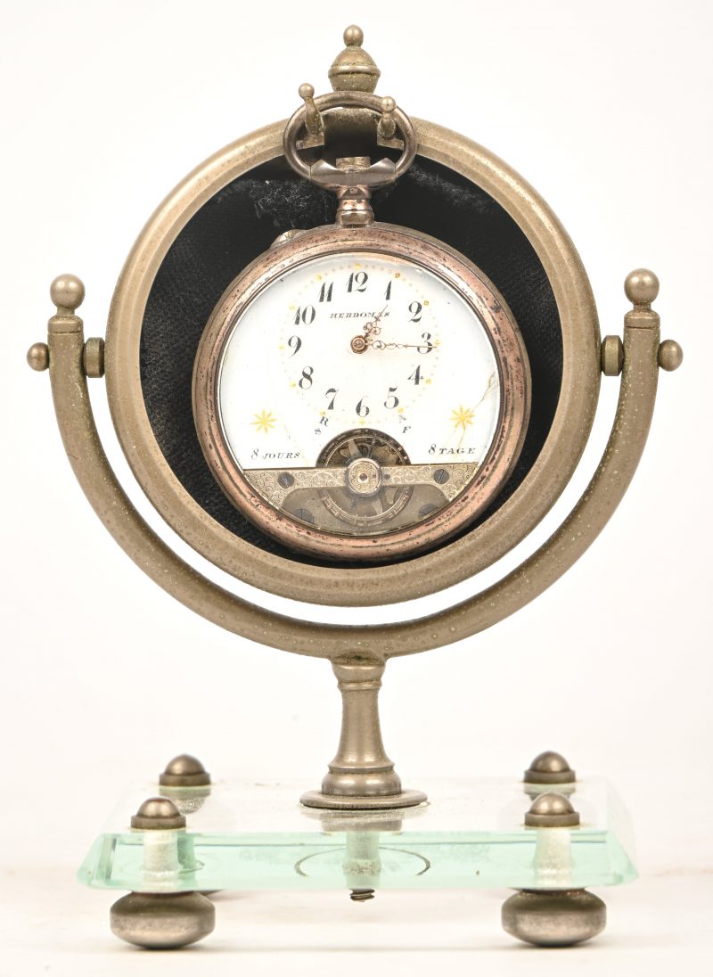 Een zilveren 8-dagen zakhorloge, Hebdonas, beschadigde wijzerplaat en ontbrekende delen. Duits gemerkt met halve maan en kroon, gehalte 800‰. Toegevoegd een metalen horlogehouder op glazen voet.