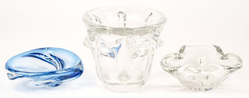 Een lot van drie voorwerpen van VSL kristal. Een kleurloze asbak, een kleine schaal, blauw in de massa gekleurd en een organisch gevormde vaas.