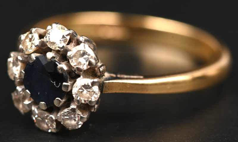 Een 18 kt wit en geelgouden ring bezet met een centrale saffier van +- 0,25 ct. en diamanten met een gezamenlijk gewicht van +- 0,40 ct.