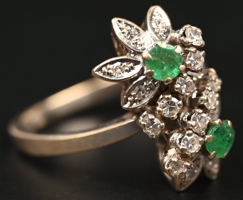 Een 18 kt witgouden ring bezet met diamanten met een gezamenlijk gewicht van +- 0,40 ct. en twee smaragden met een gezamenlijk gewicht van +- 0,20 ct.