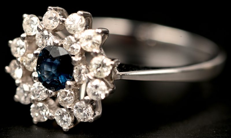 Een 18 kt witgouden ring bezet met diamanten met een gezamenlijk gewicht van +- 0,30 ct. en een centrale saffier van +- 0,20 ct.