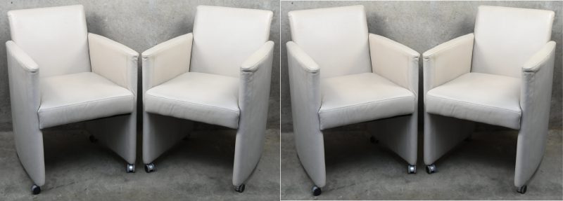 Een set van vier eetkamerstoelen op wieltjes, met armleuningen. Met ecrukleurige skai bekleding.