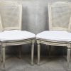Een set van vier eetkamerstoelen met cannage zit en rug, stijl Louis XVI. Lichtgrijs gepatineerd, met bijpassende kussens.