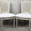 Een set van vier eetkamerstoelen met cannage zit en rug, stijl Louis XVI. Lichtgrijs gepatineerd, met bijpassende kussens.