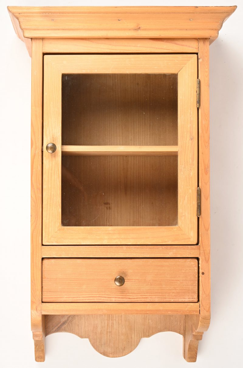 Een klein grenenhouten hangkastje met een vensterdeur en 1 lade.