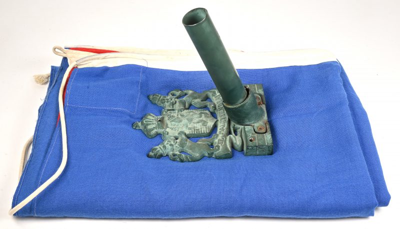 Gietijzeren vlaggenstokhouder. Met het wapenschild van het Koninkrijk der Nederlanden. Toegevoegd een Nederlandse vlag.