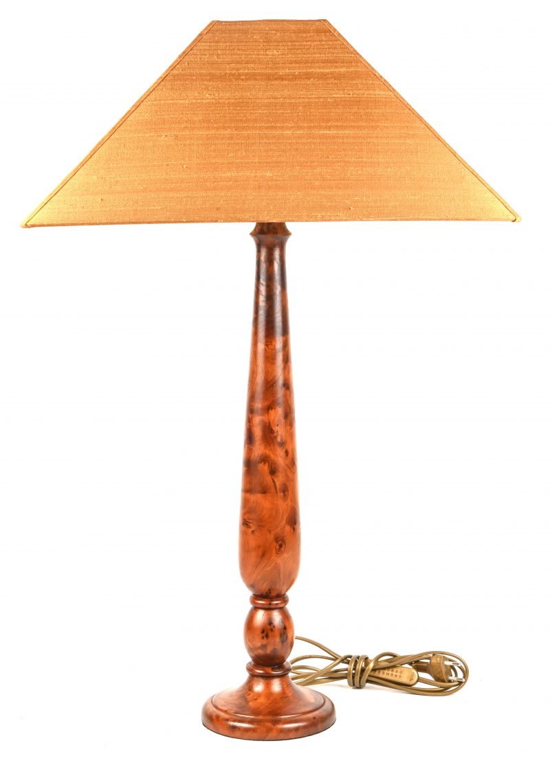 Een tafellamp, houten voet en bronskleurige lampenkap.