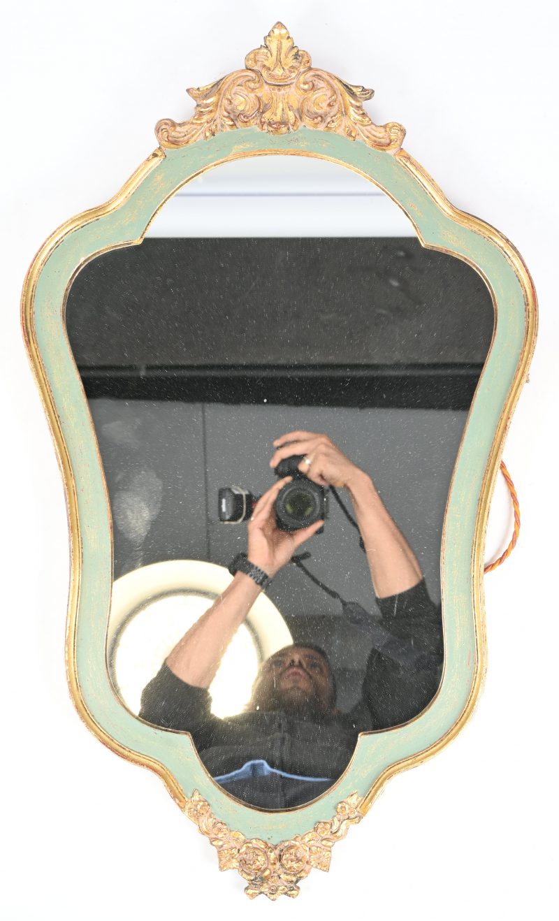 Een kleine spiegel in goudkleurig kader met barokke ornamenten.