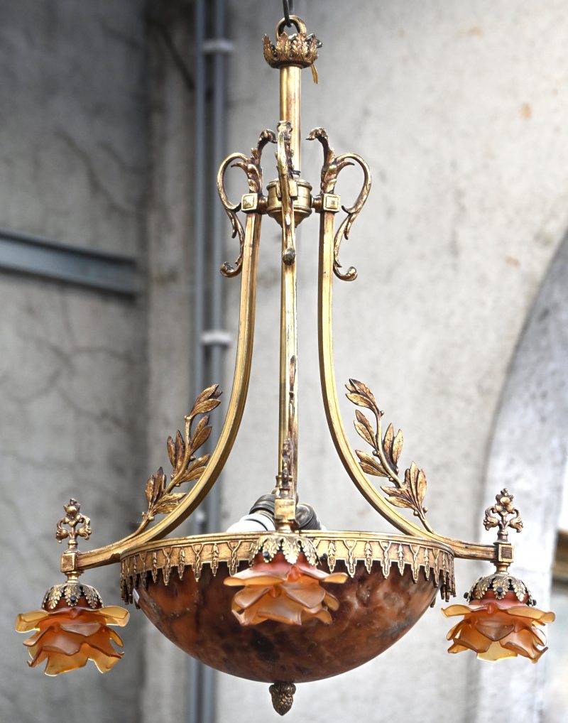 Een bronzen hanglamp met albasten coupe en drie roosvormige glazen blakers.