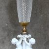 Een paar klassieke tafellampen, elk gedragen door drie dansende putti’s van bisquit. Met delen van glas en messing.