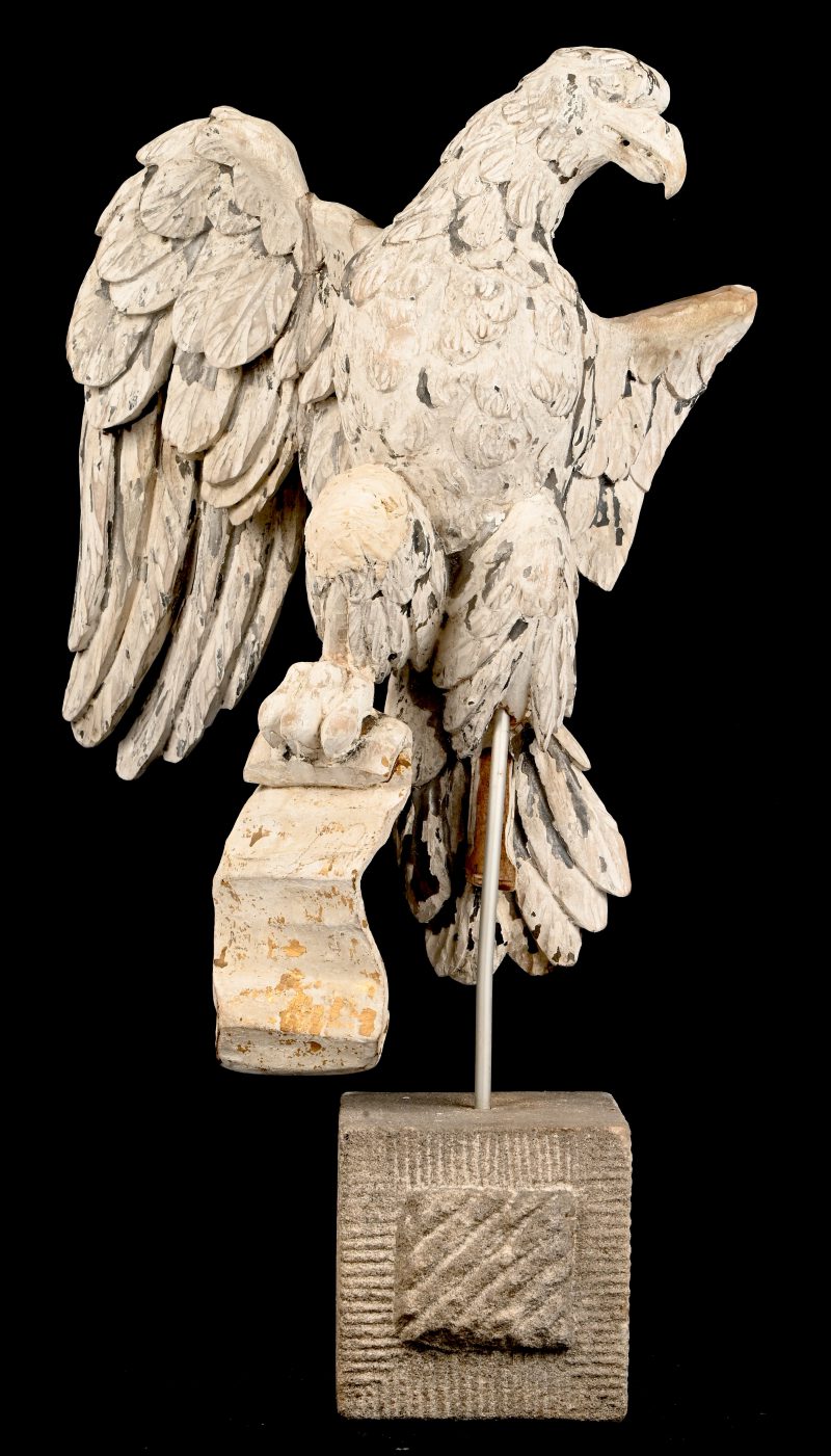 Een adelaar in hout gesculpteerd op stenen sokkel. Eén vleugel is manco.