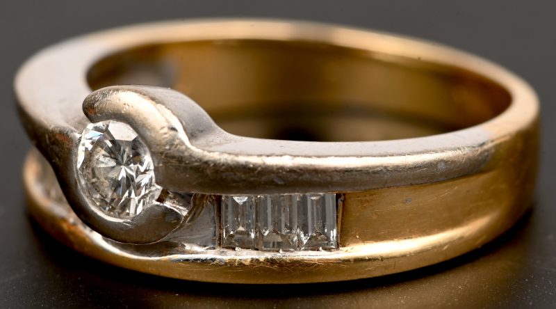 Een 18 kt wit en geelgouden ring bezet met een centrale briljant van +- 0,20 ct. en baguetten met een gezamenlijk gewicht van +- 0,20 ct.