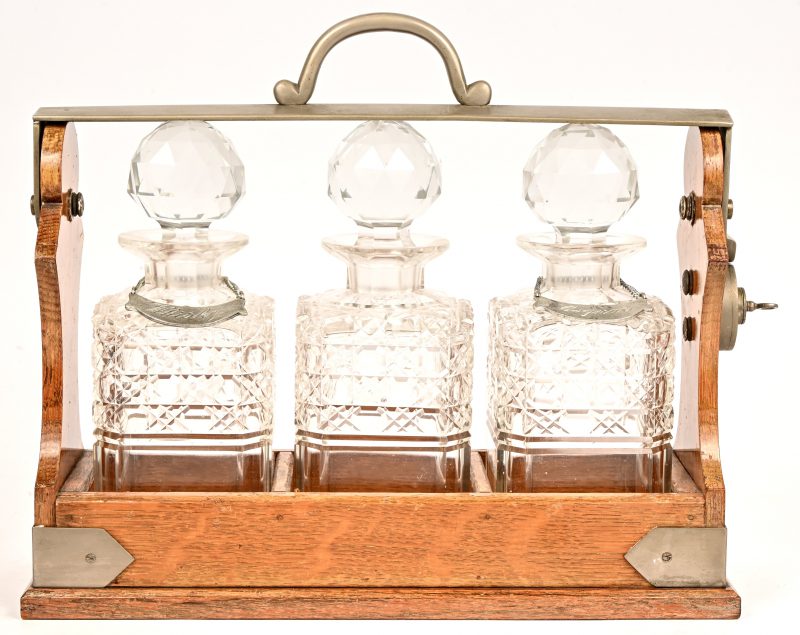 Een tantalus van eik, metaal en met drie karaffen van kristal. Gemerkt “The Tantalus”.