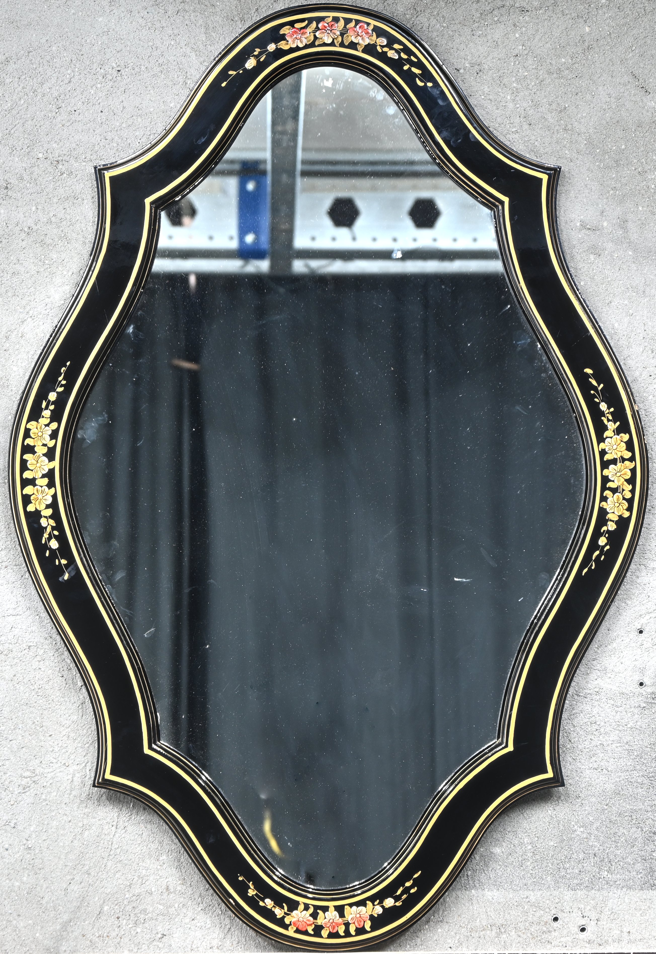 Een spiegel in zwart gelakte kader met florale decoratie Een spiegel in zwart gelakte kader met florale decoratie.