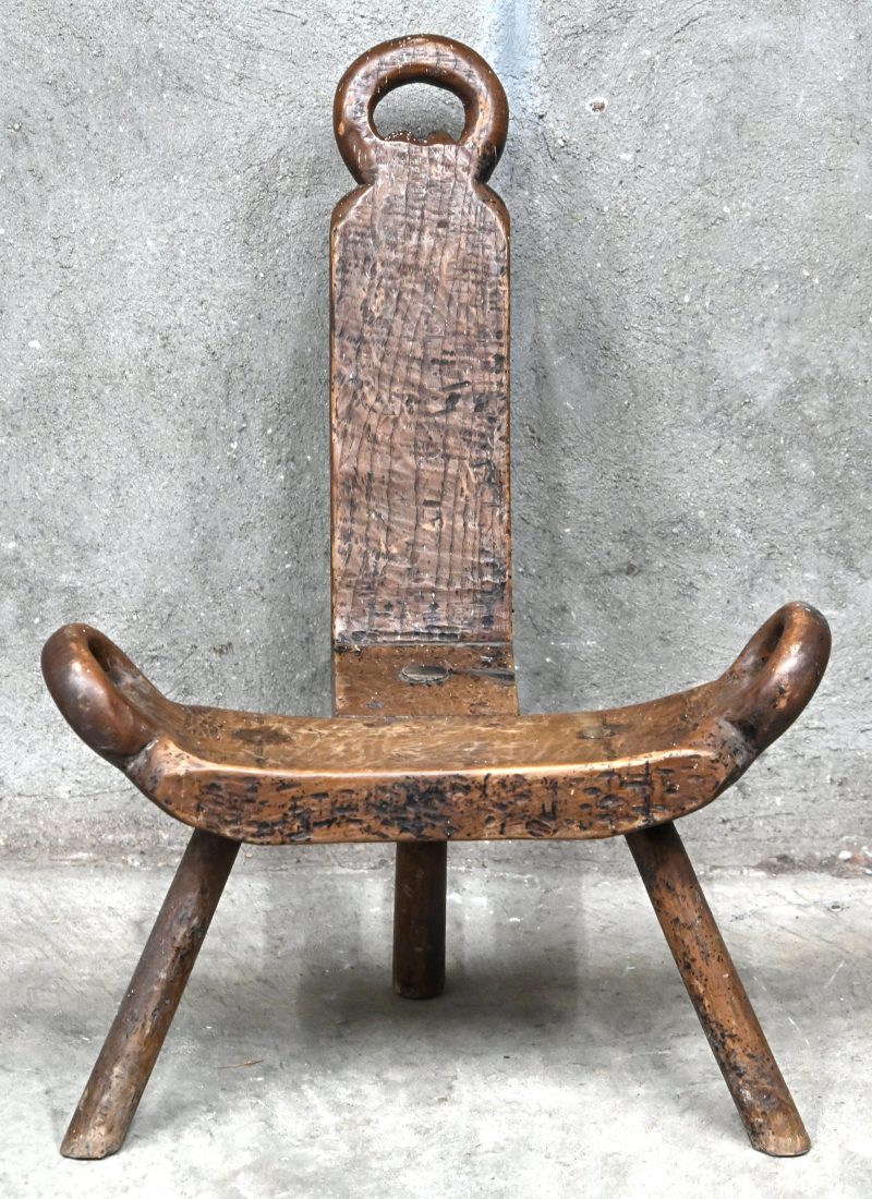 Een massief houten melkstoeltje op drie poten, rustieke stijl.