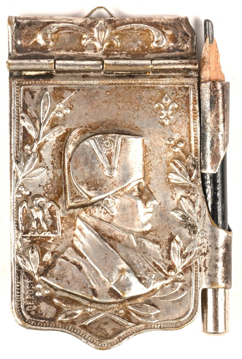 Een zilveren houder voor een notitieboekje met potlood gedecoreerd met de buste van Napoleon en hierin mini foto’s van deze man. 15 gram bruto.