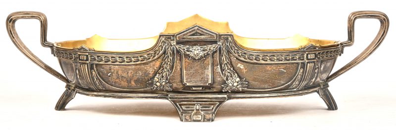 Een grote langwerpige milieu de table van gedreven zilver. Duitse keuren, 800/1000. Messingen binnenschaal. Decor met guirlandes. Opschrift m.b.t. een jubileum in het Osterriethuis in 1911.