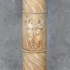 Een zuil van monochroom beige aardewerk met een reliëfdecor van personages naar de Griekse oudheid.