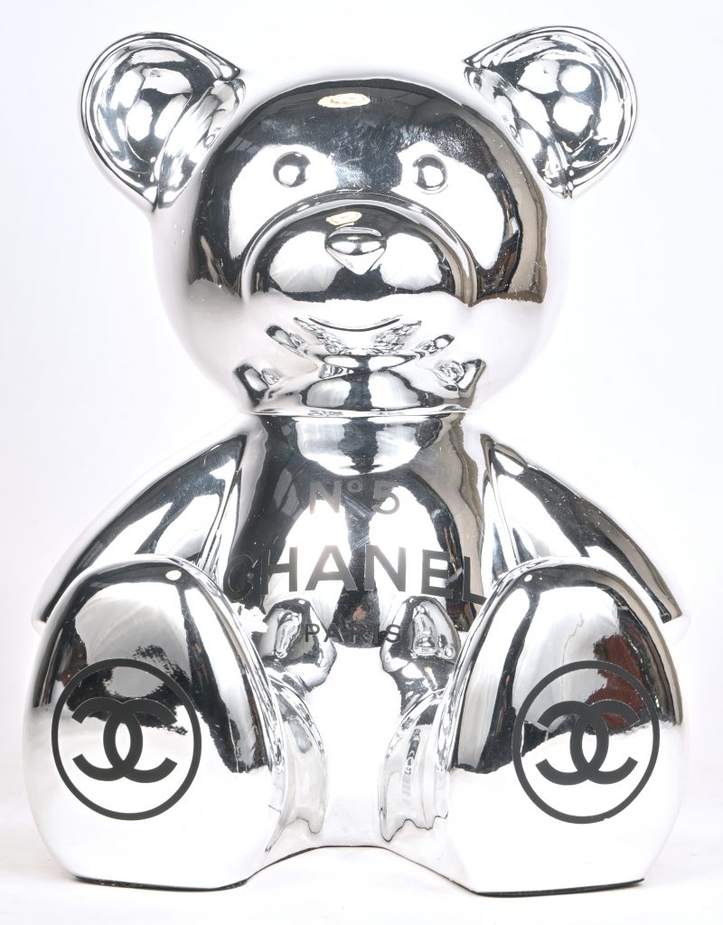 “Een Teddy Chanel”. Een zilverkleurig beeld van een beer met logo van parfum Nr. 5. In originele doos. (heeft een wit vlekje tussen de bil).