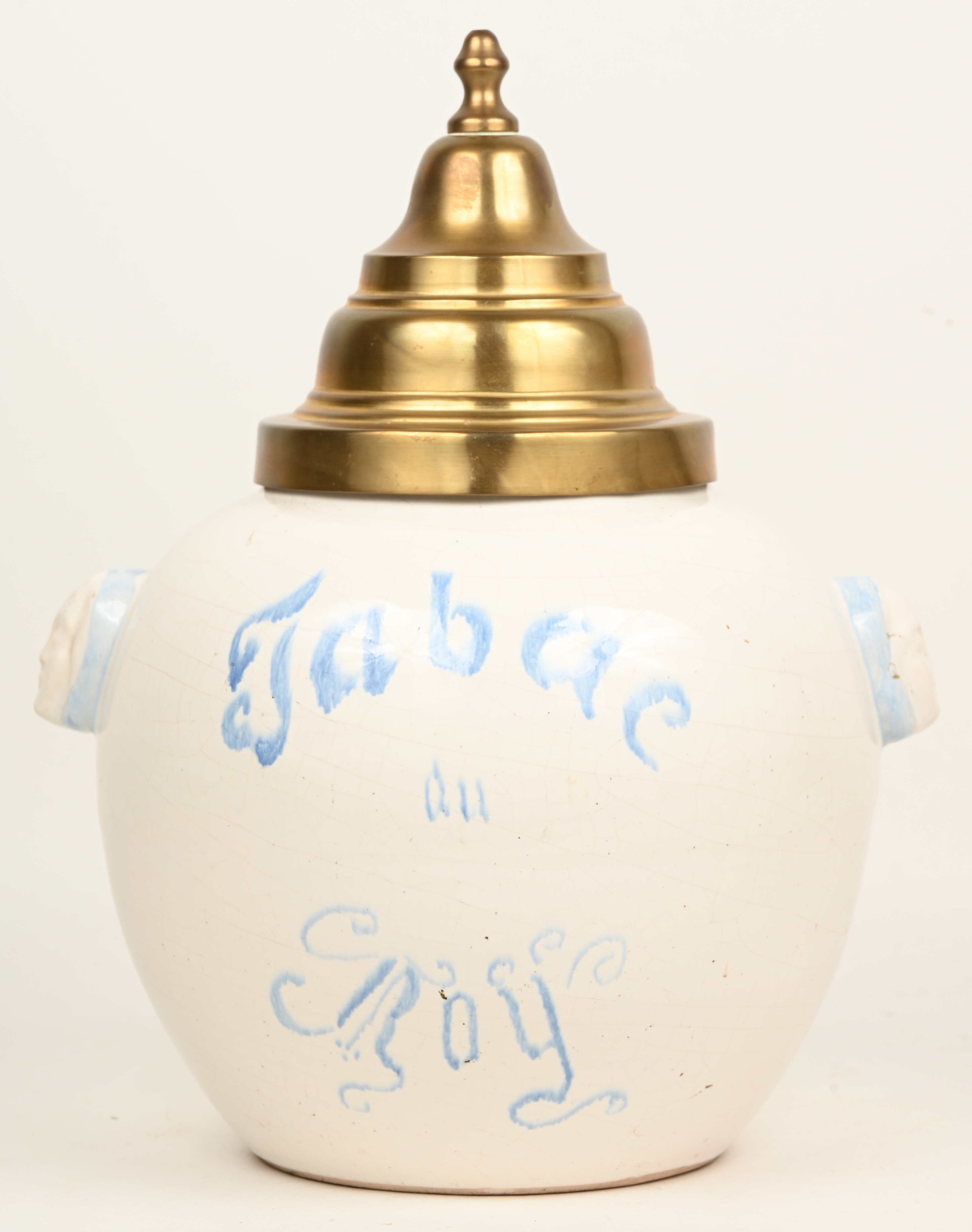 Een porseleinen tabakspot met koperen deksel en gezichten in het handvatreliëf. Opschrift “Tabac au Roy” Een porseleinen tabakspot met koperen deksel en gezichten in het handvatreliëf. Opschrift “Tabac au Roy”.