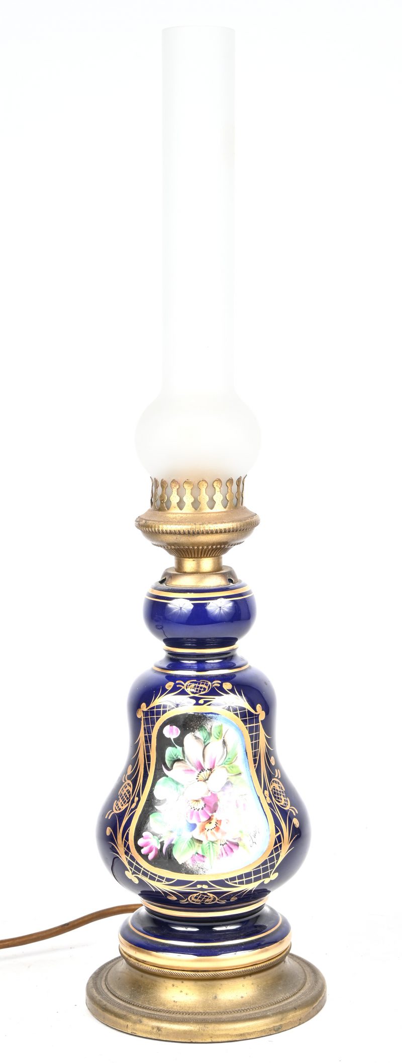 Een olielamp van kobaltblauw porselein met bloemendecor en met koperen monturen. Met lampenglas. Op elektriciteit.